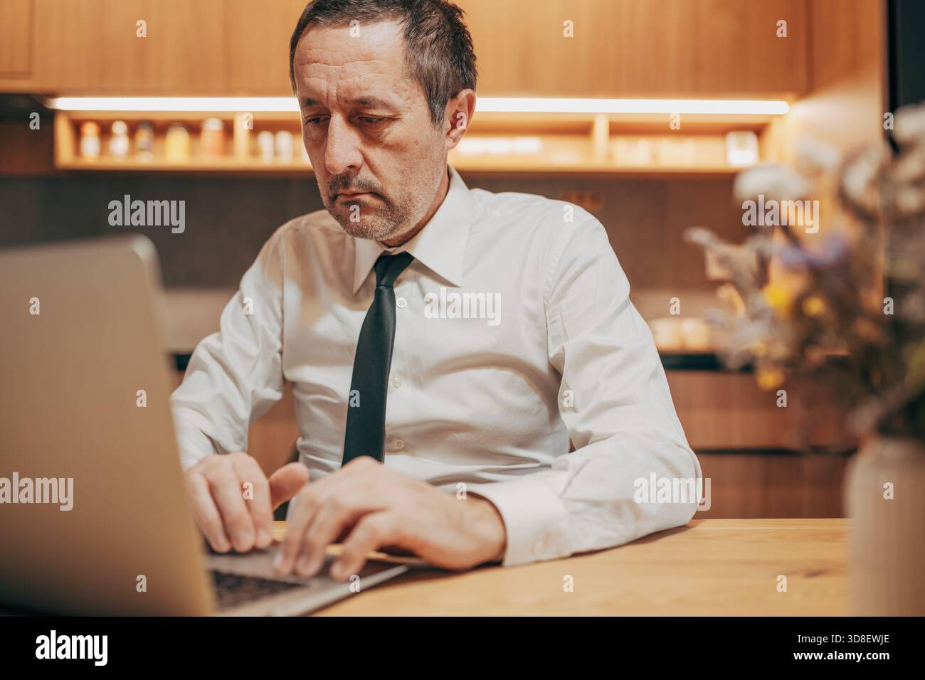 Professional man in formal attire using a laptop in a home office environment, concentrating on work. Selective focus. Stock Photo