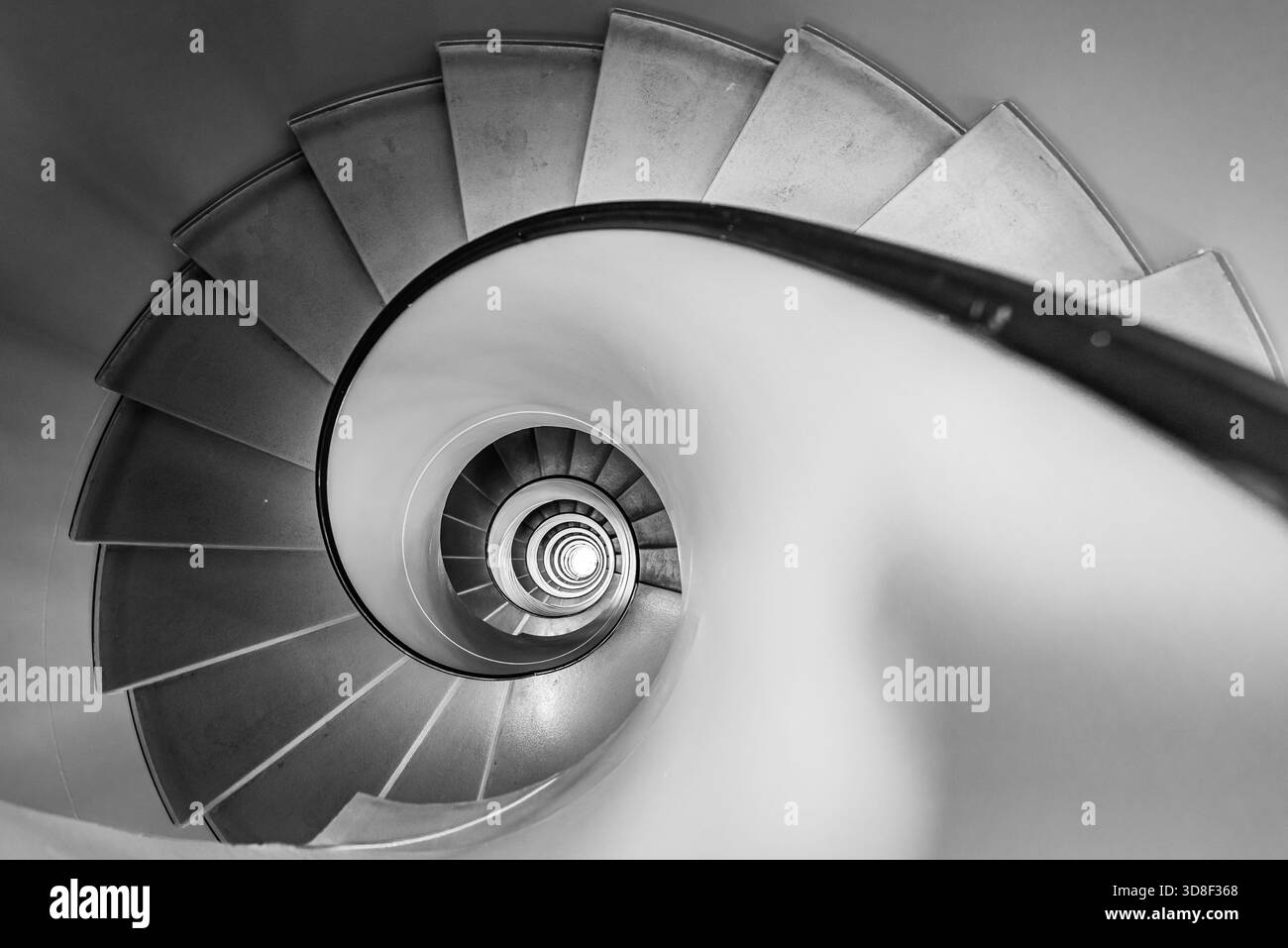 Overhead view of a grey spiral staircase in Geneva, Switzerland. The black and white architectural image shows a descending circular flight of steps. Stock Photo