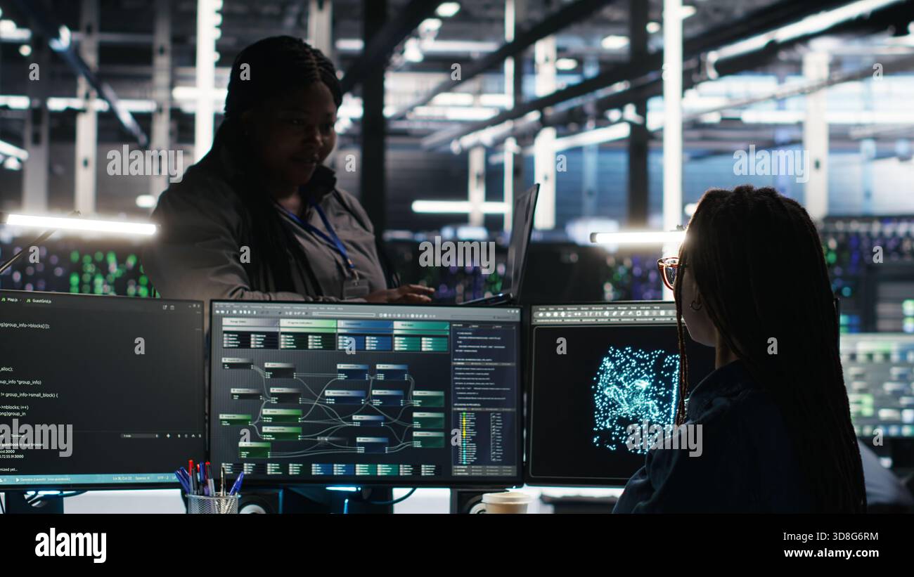 Data center manager supervising technician using node tree software to analyze datasets. Server room team leader oversees IT expert using visual programming tools to improve gear performance, camera B Stock Photo