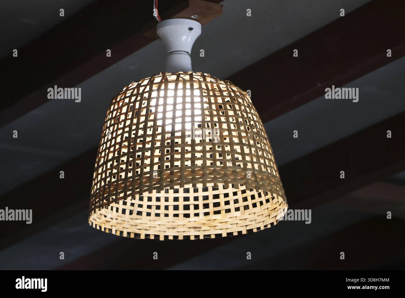 Cozy warm rustic lamp with handmade bamboo wicker light shade. beautiful interior decoration creating an inviting atmosphere hanging from dark ceiling Stock Photo