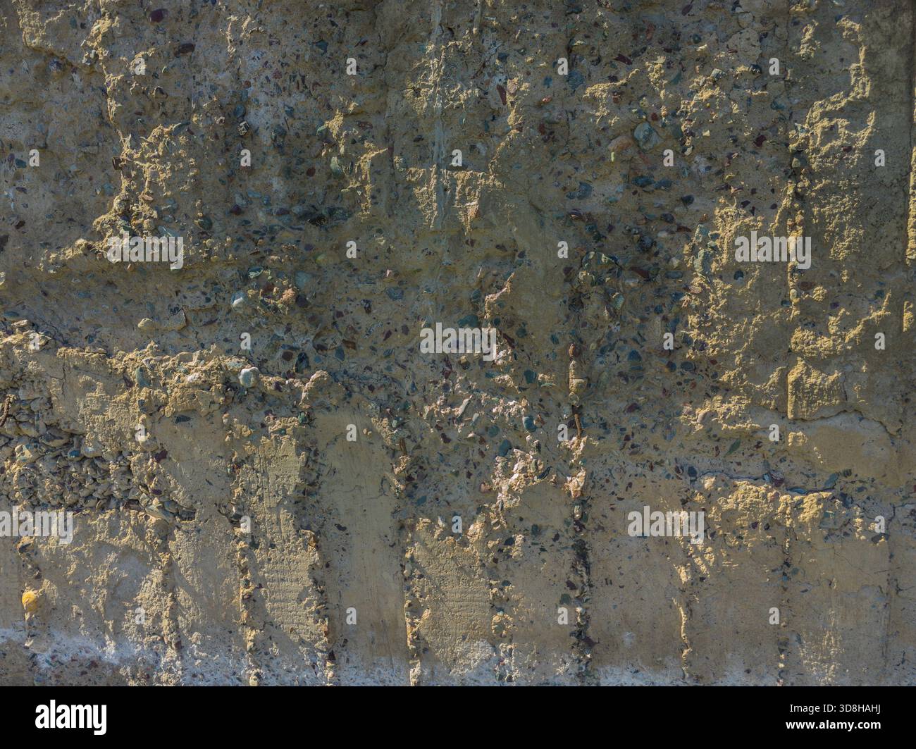 Rough, uneven concrete surface embedded with small pebbles and showing signs of age and wear under tangential harsh sun light showing all imperfections. Stock Photo