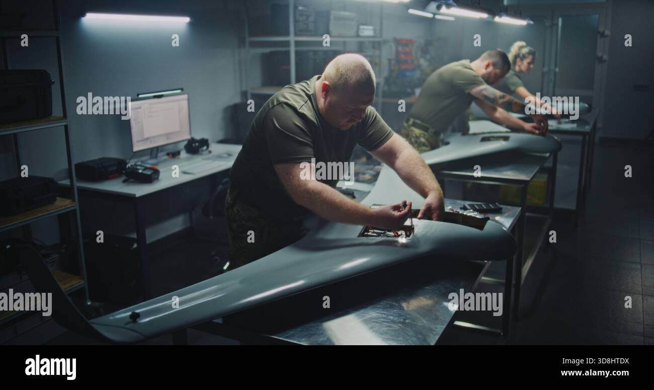 Installing Flight Electronics Technician Working on UAVs Core. Team in Uniform Installing or Checking Complex Flight Electronics Inside Body of UAV. Precision Required For Military Drone Systems. Stock Photo