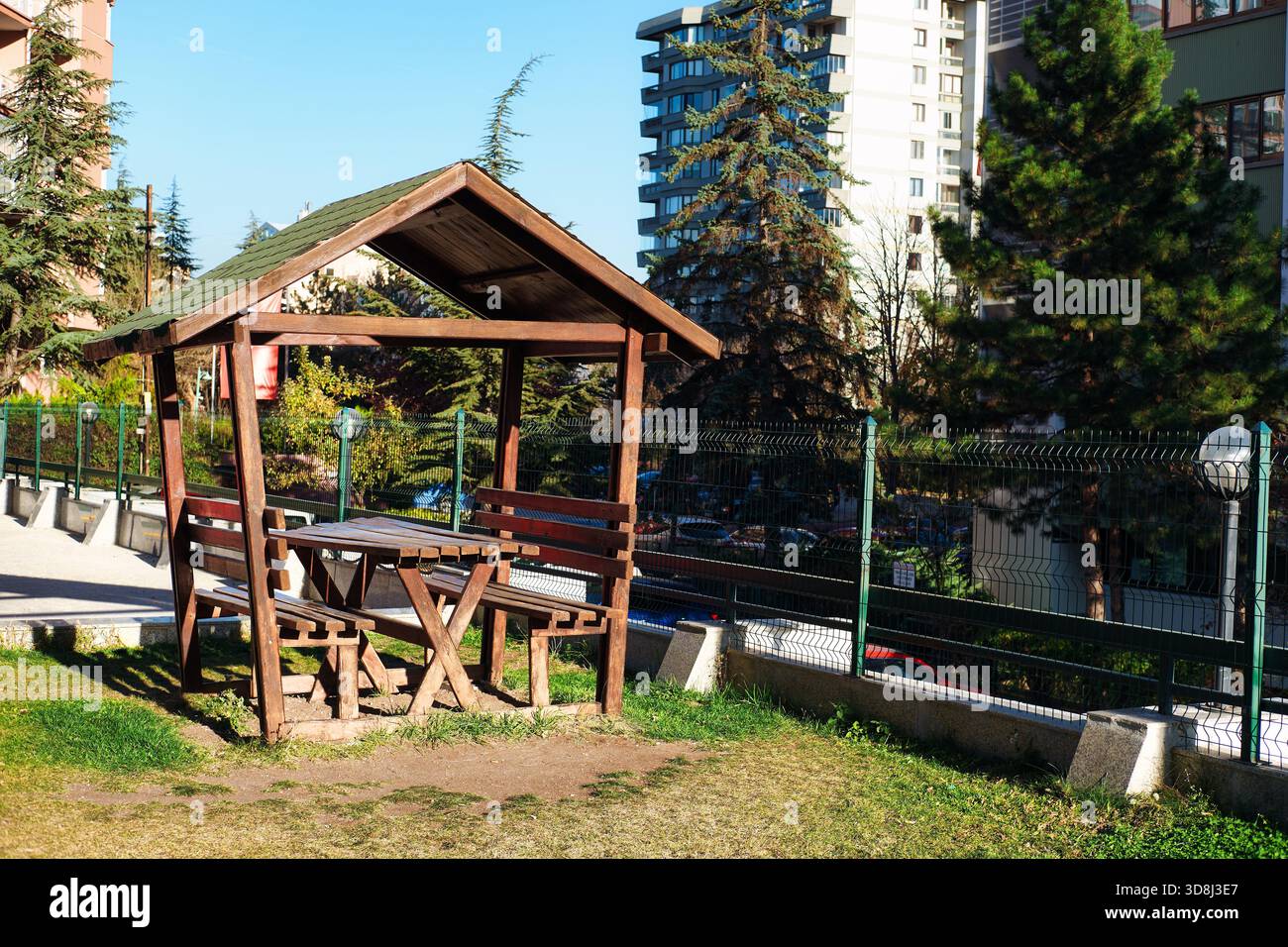 Wooden gazebo structure with picnic table and benches on grass in an ...