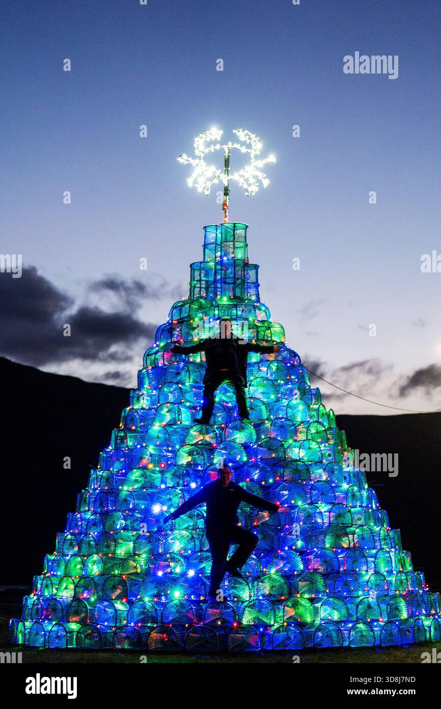 Volunteers George Holroyd (top) and Colin Boyle (bottom) check the lights on the fishing creel Christmas tree they helped to build on the harbour-side in Ullapool, Wester Ross. The 30ft tree, made using 340 creels used for catching crabs and prawns, has become a tradition in Ullapool since it was first constructed in 2016. Picture date: Sunday November 30, 2025. Stock Photo
