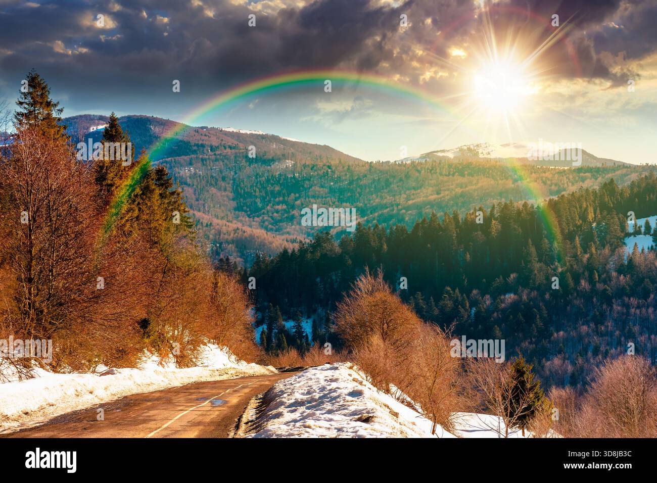 country road winding through winter landscape under blue sky at sunset. mountains in evening light. travel background with snow covered slopes. storyt Stock Photo