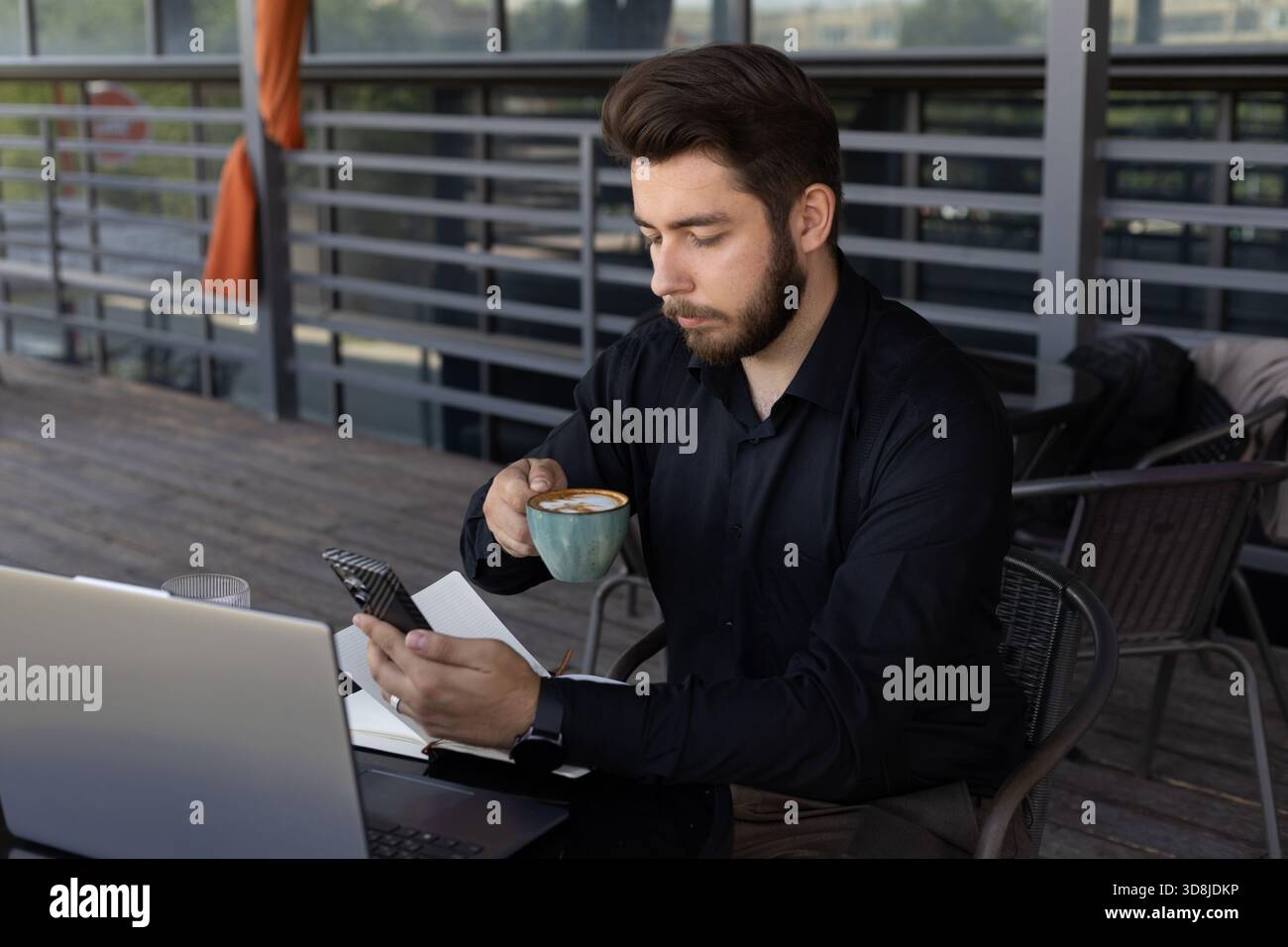 A man is drinking from a mug while using his smartphone. Stock Photo