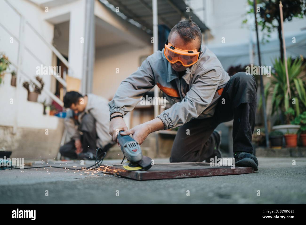 Construction worker using an angle grinder outdoors with safety goggles, sparks flying Stock Photo