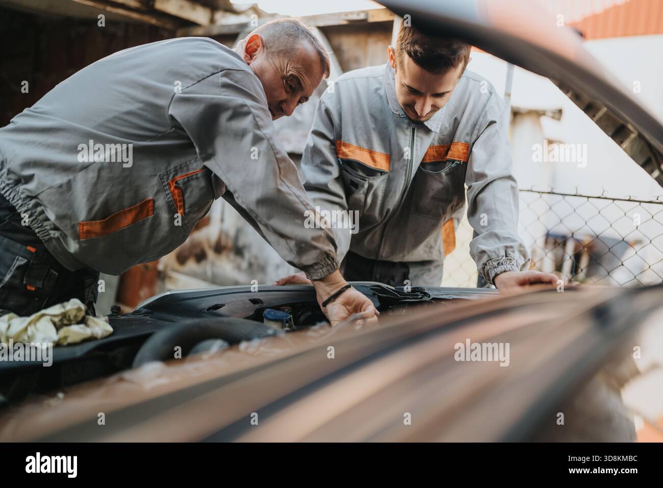 Two mechanics inspect a car engine under the hood, teamwork and repair in progress Stock Photo