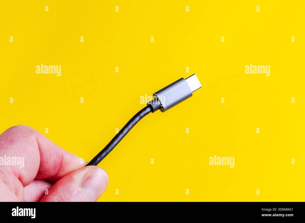 USB-C cable held in hand against a bright yellow background Stock Photo