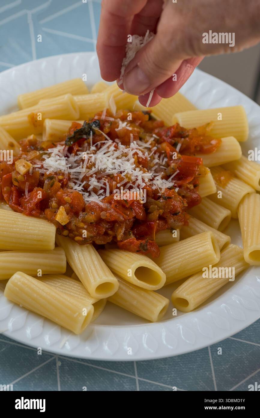 Adding cheese to a plate of macaroni with tomato sauce Stock Photo