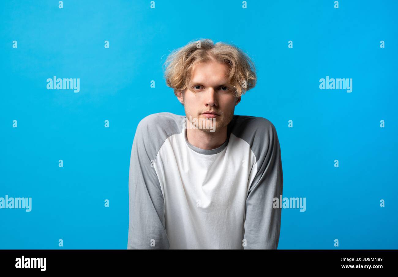 Thoughtful young man leaning slightly forward with serious expression on bright blue background Stock Photo