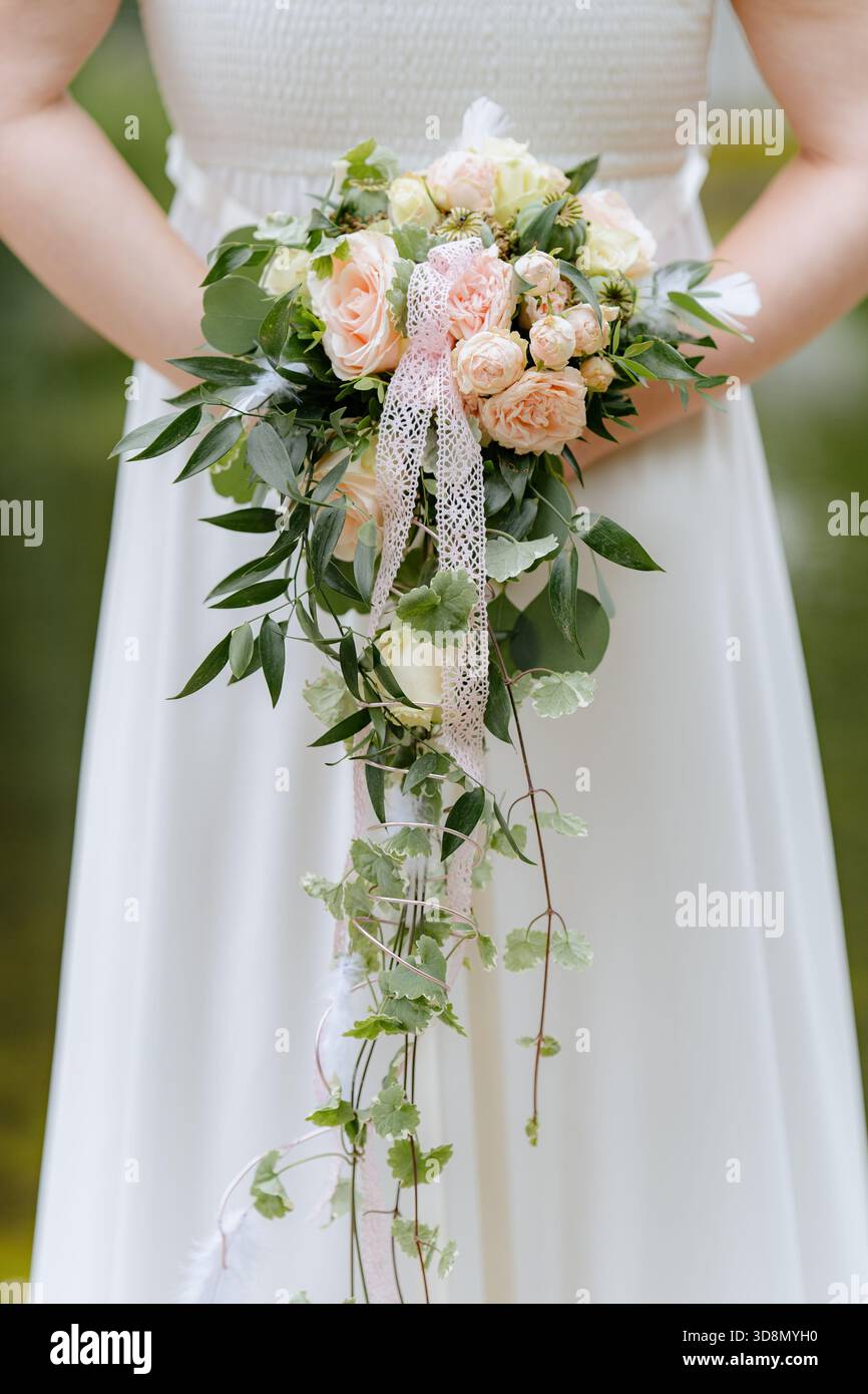 Close-up of a bride in white dress holding a romantic cascading bouquet  with pastel roses, greenery, and lace ribbon Stock Photo - Alamy