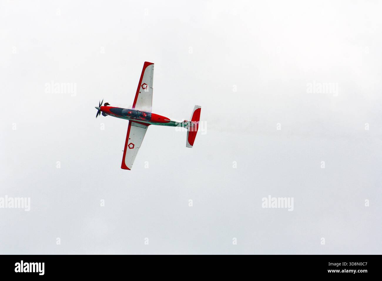 Aerobatic plane soars through cloudy skies with precision turns, leaving a trail of excitement for spectators below. Stock Photo