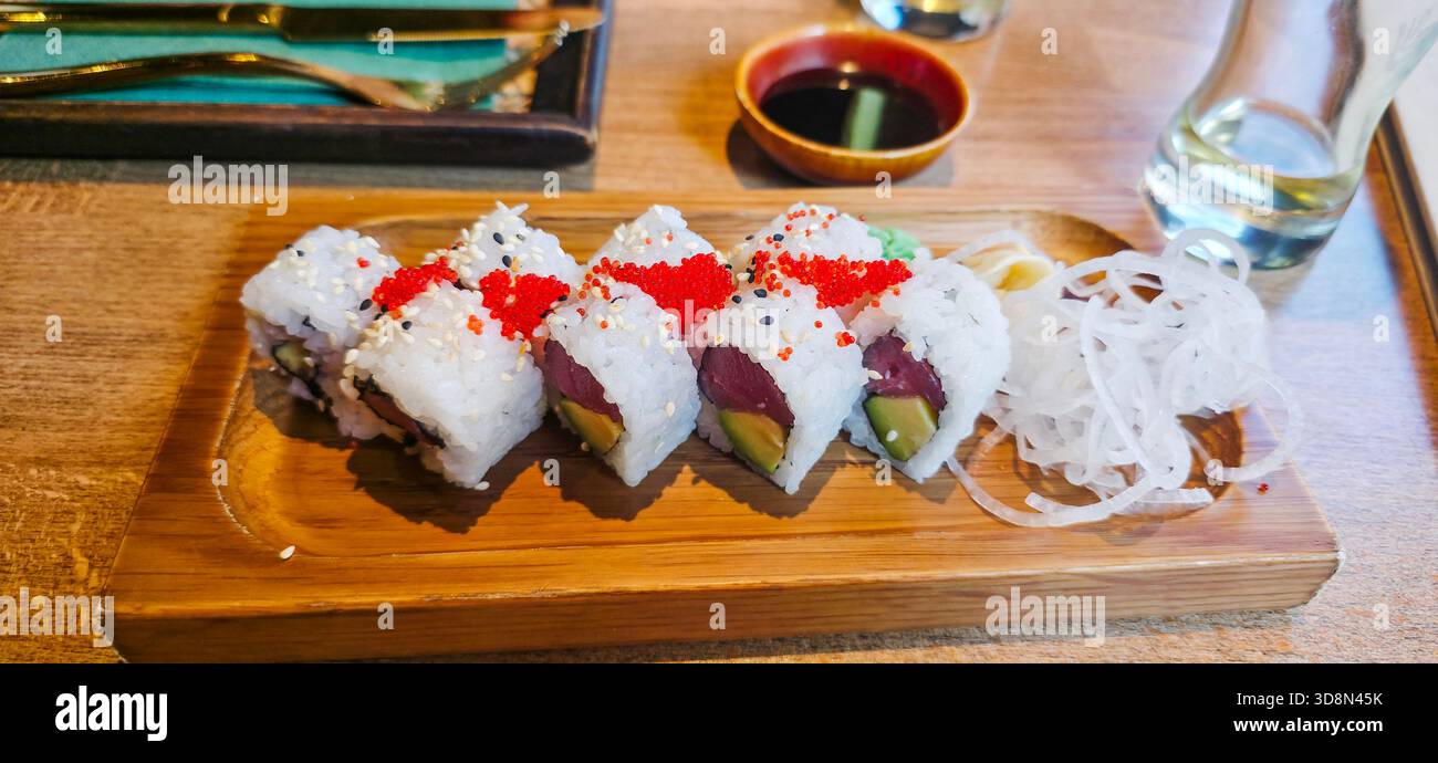 Colorful sushi rolls are beautifully arranged on a wooden plate, accompanied by dipping sauce and garnishes, showcasing culinary artistry. - Smartphone Captured Stock Image