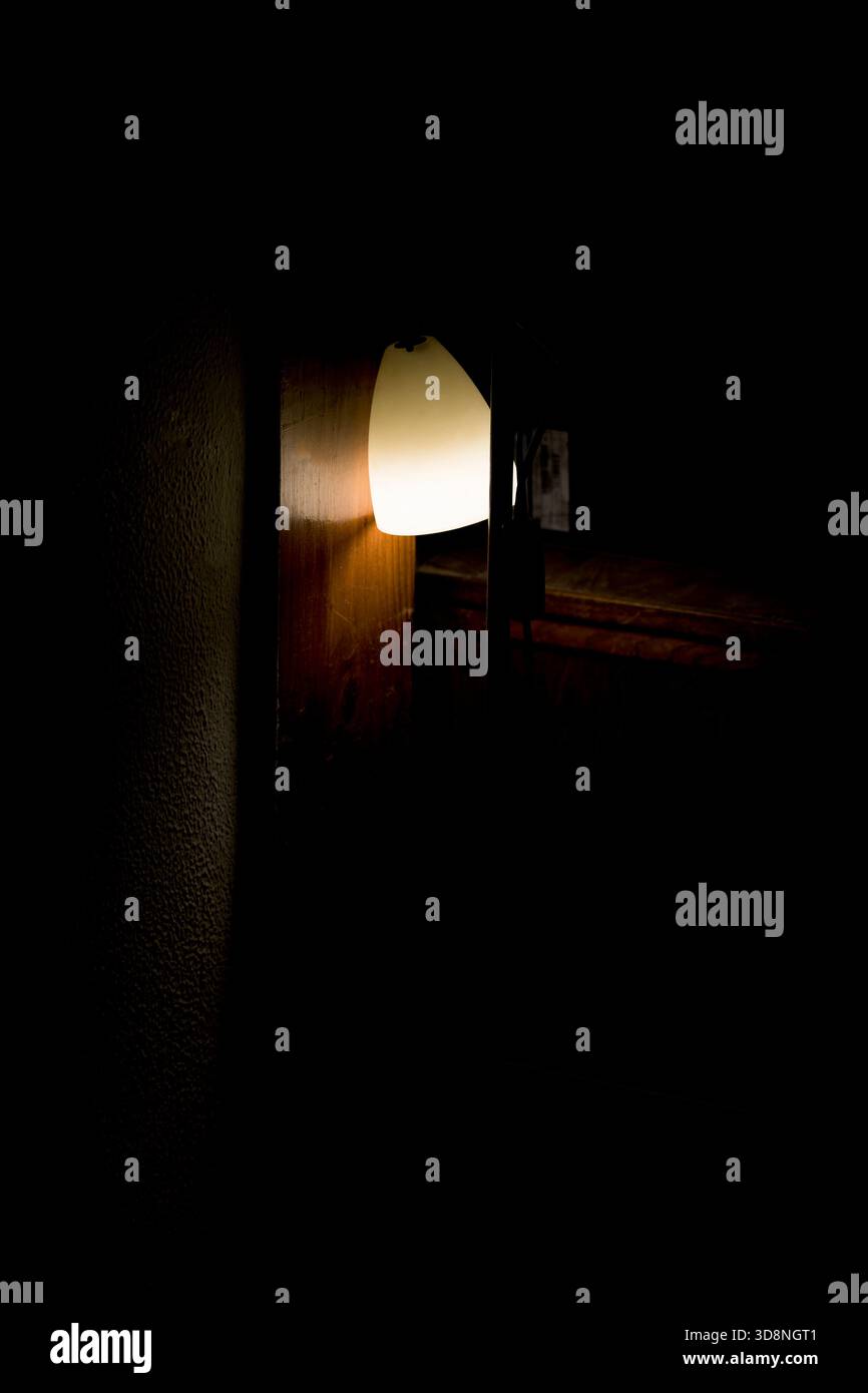 Close up shot of a minimalist vertical floor lamp emitting a soft, warm, and comforting glow in a dark room. The lighting creates a cozy and peaceful Stock Photo