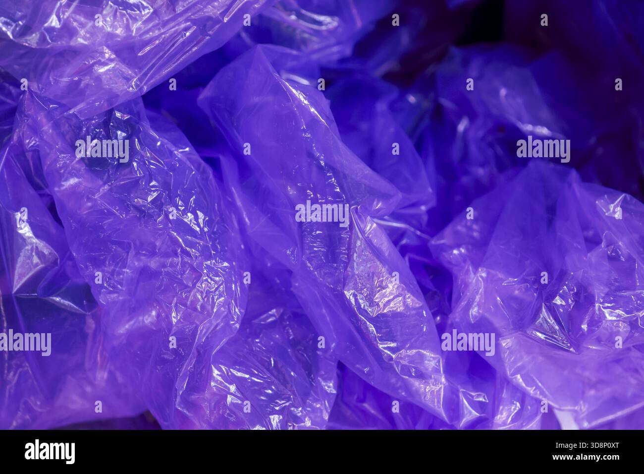 Mysterious purple light glow on crinkled plastic bag pile. An abstract background texture of translucent packaging with dark, clandestine and futurist Stock Photo