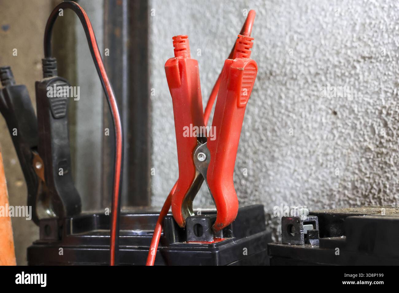 Red positive clamp from booster cable attached to car battery terminal ...