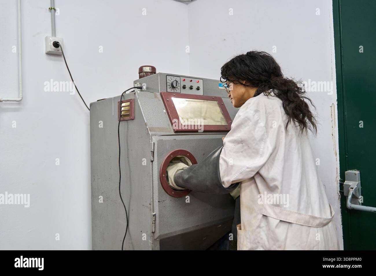 Female worker using a sandblaster machine in a lab setting, focused on a technical process. Industrial expertise Stock Photo