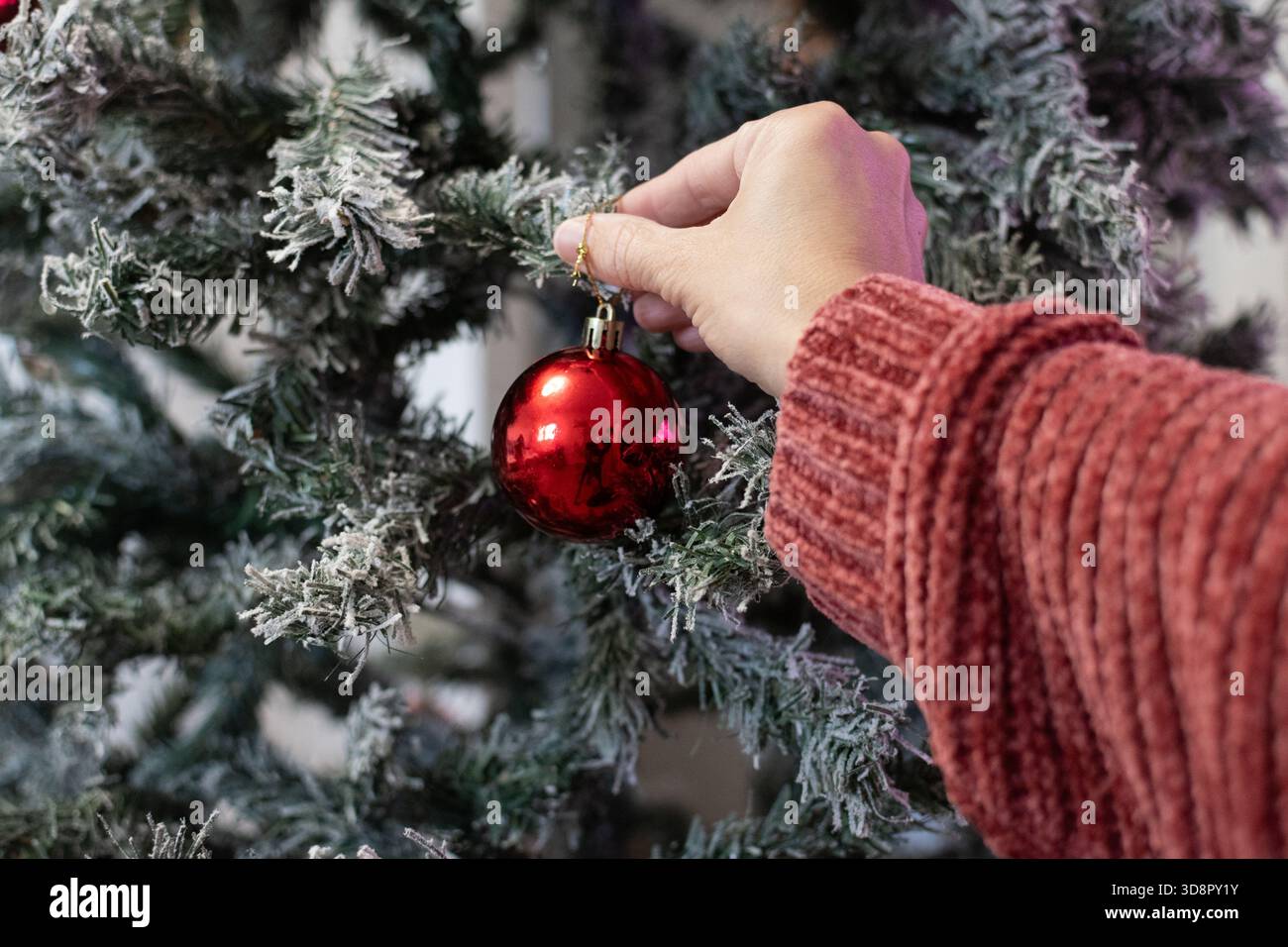 Close-up of a woman’s hand placing a Christmas ornament on a decorated tree Stock Photo