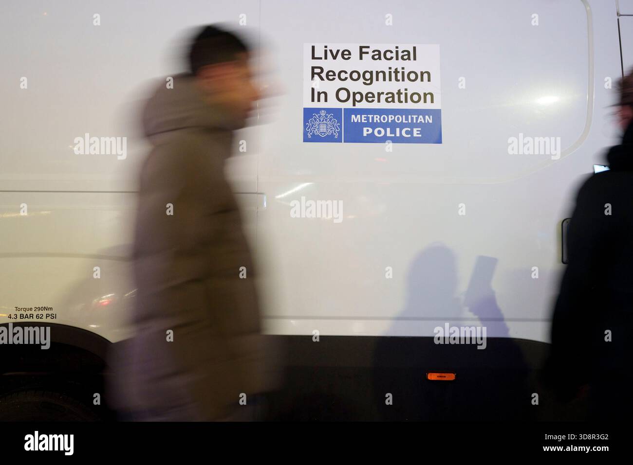Shoppers walk past a Met police van that's using Artificial Intelligence (AI) Facial Recognition (FI) technology to spot persons of interest, and pre-empt criminal activity, at Tottenham Court Road, on 1st December 2025, in London, England. Facial Recognition (FR) technology is used by the Met to prevent and detect crime, find wanted criminals, safeguard vulnerable people. Real time surveillance helps officers locate people on a ‘watchlist’ who are sought by the police. FR cameras focus specific areas and when people pass through, their images are streamed directly to the Live Facial Recognit Stock Photo