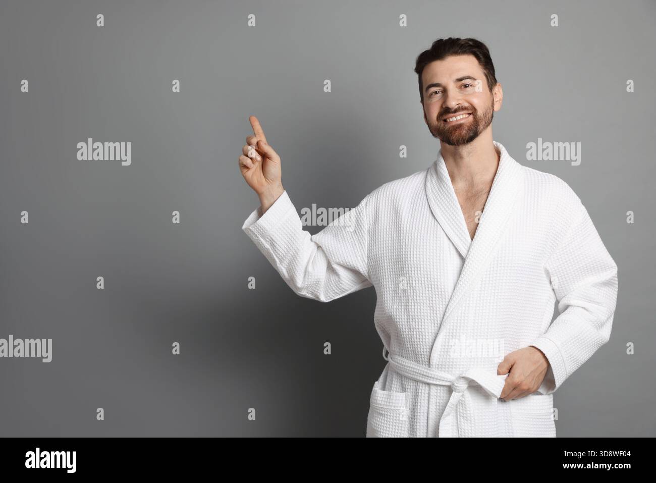 Man in bathrobe pointing at something on grey background. Space for text Stock Photo