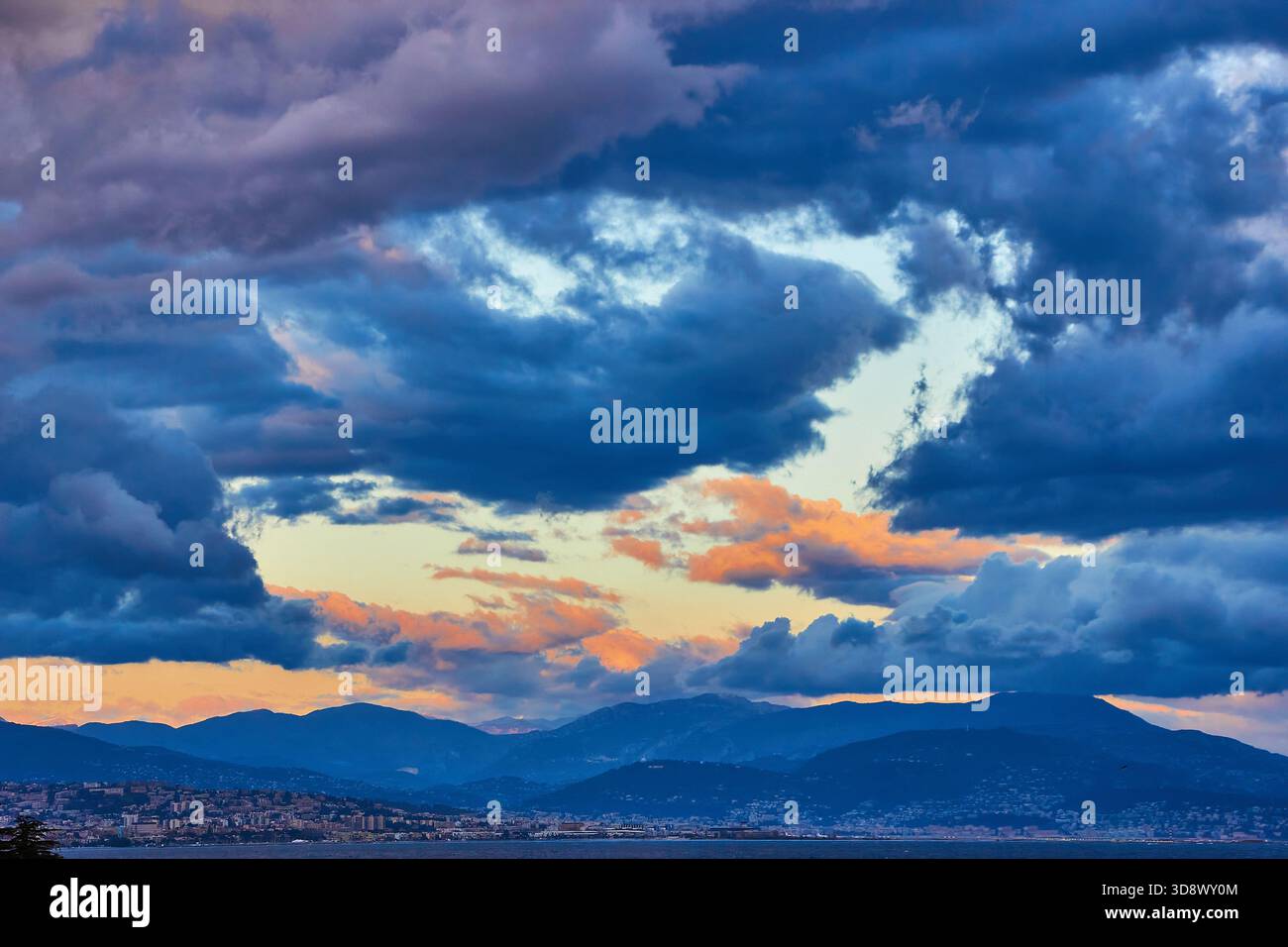 Dramatic Sunset Over Cloudy Sky, Mountain Range, And City Skyline Stock Photo