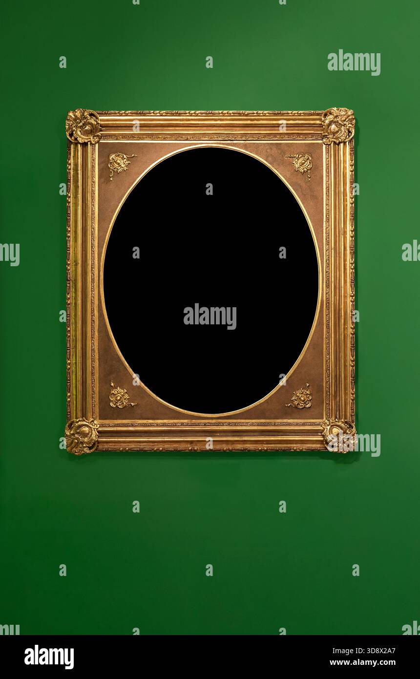 Ornate golden rectangular frame with an oval opening hanging on a solid green wall. Stock Photo