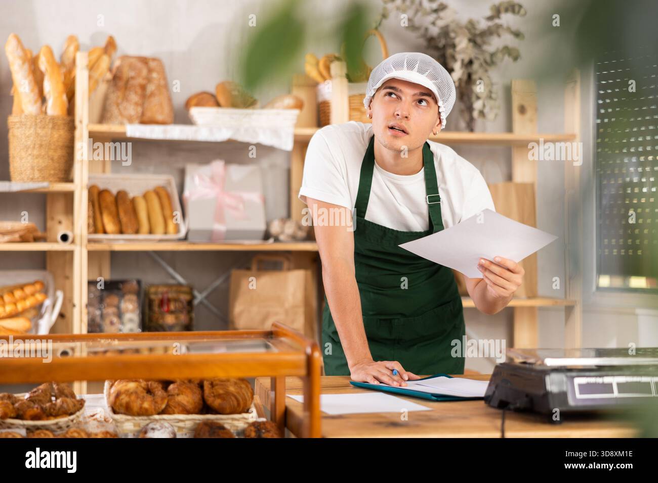 Thoughtful young baker looking over papers in craft bakery Stock Photo