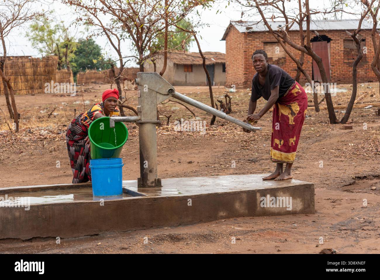 Salima Malawi southern Africa. 15.11.2025.  Malawian women dressed in colourful wrappers drawing fresh water by a borehole pump. - Stock Image