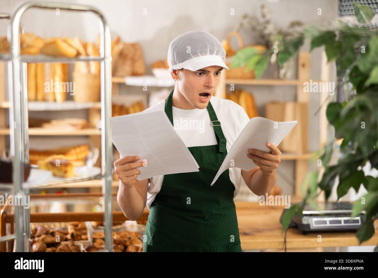 Young baker looking confused while reviewing order documents Stock Photo