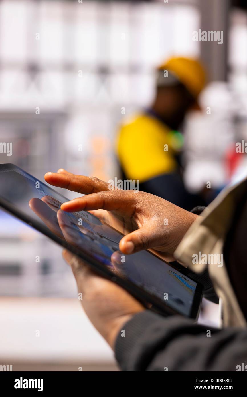 Industry 4.0 engineer programs automated assembly line and robot arm using CAD software on tablet. African American automation specialist employs digital interface to control advanced manufacturing. Stock Photo