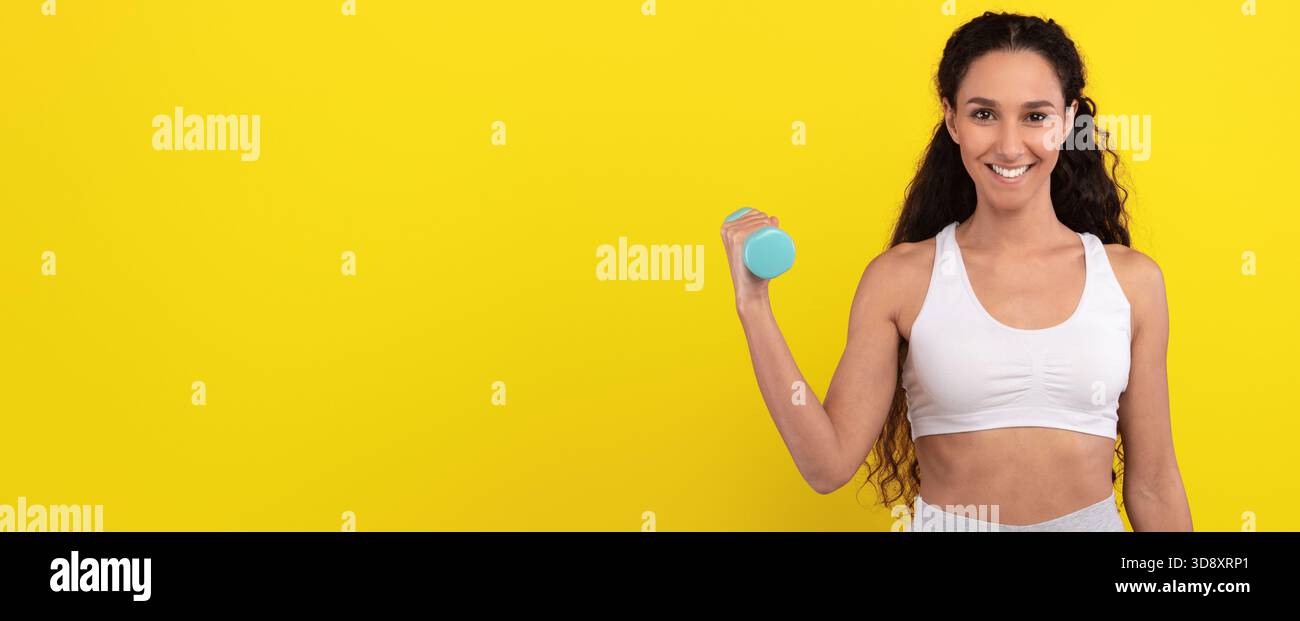 Woman Exercising With Dumbbell Against Bright Yellow Background During Fitness Routine Stock Photo