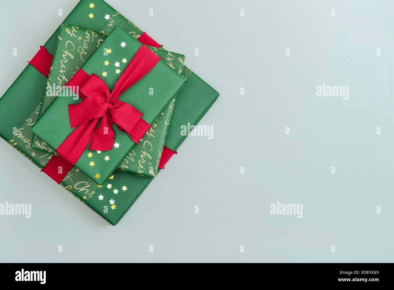 Stack of green gift boxes with red ribbon and golden and silver  star-shaped confetti  on blue background, top view Stock Photo