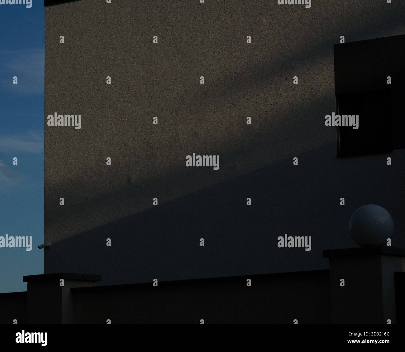 Shadows on the wall of a white house, a slice of blue sky Stock Photo