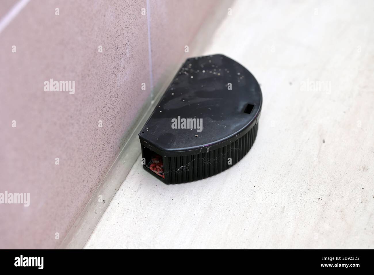 A rodent bait station placed on the floor near the wall. Stock Photo