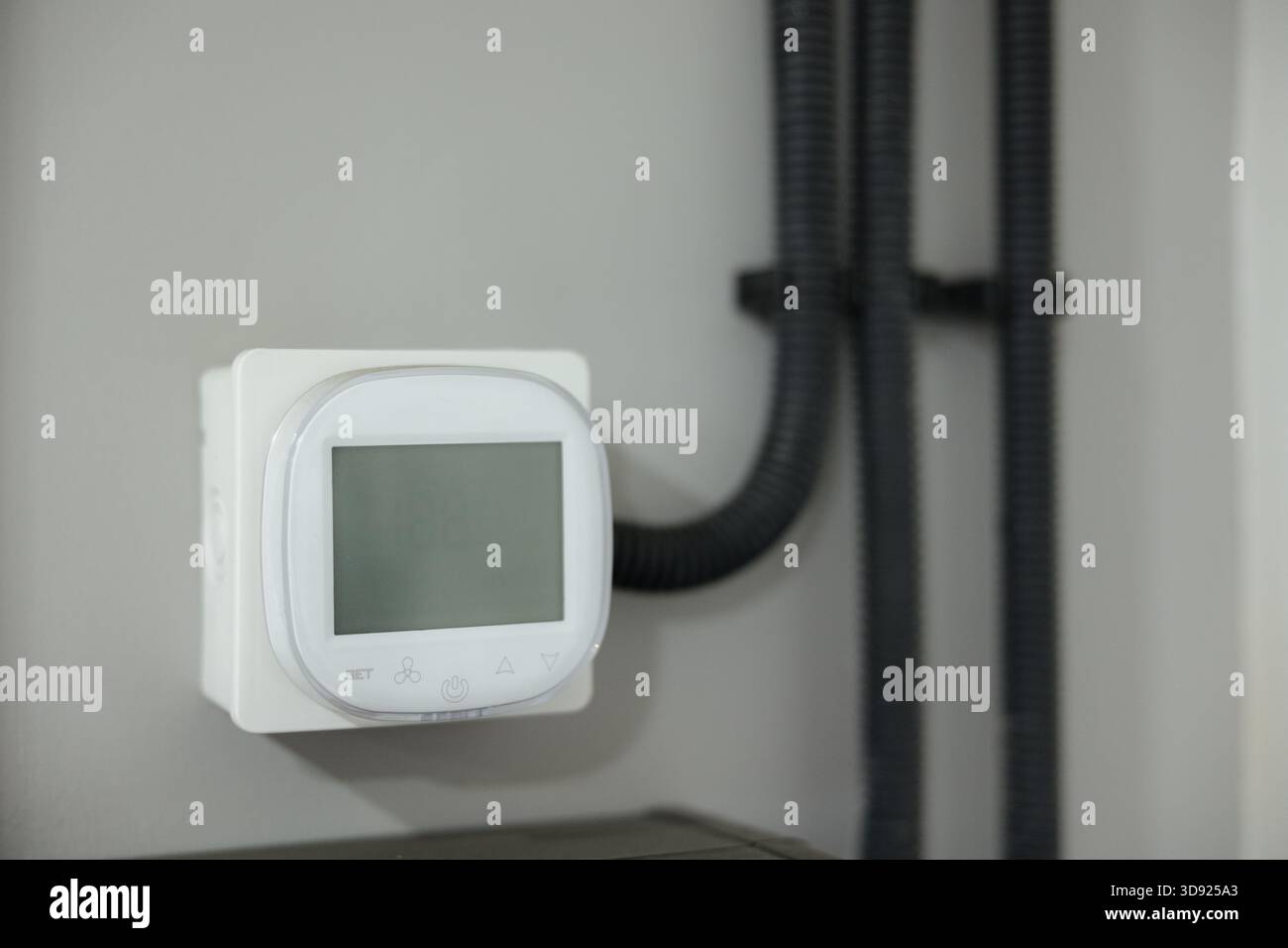 A sleek digital thermostat is mounted on a wall, programmed to maintain the perfect temperature in a contemporary living space. Stock Photo