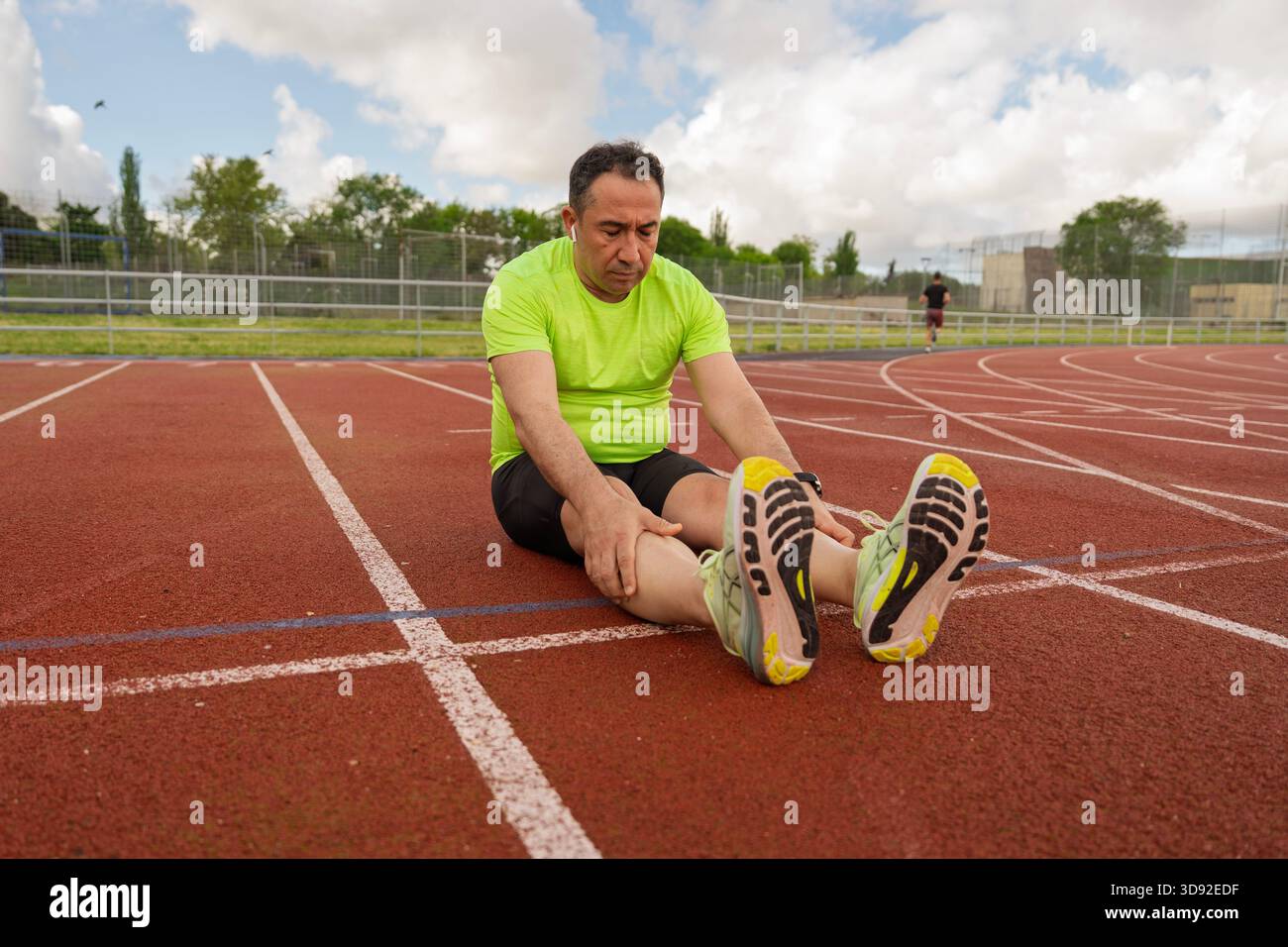 Senior athlete taking a break on track and field, stretching legs after intense training session Stock Photo