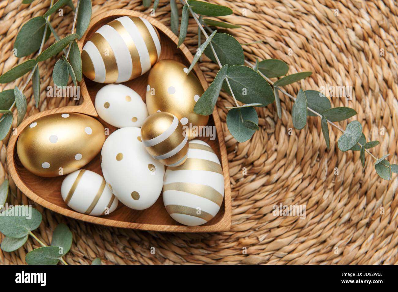 Easter decor. Easter eggs painted in gold in a heart-shaped wooden bowl. The concept of preparation for the celebration. Stock Photo