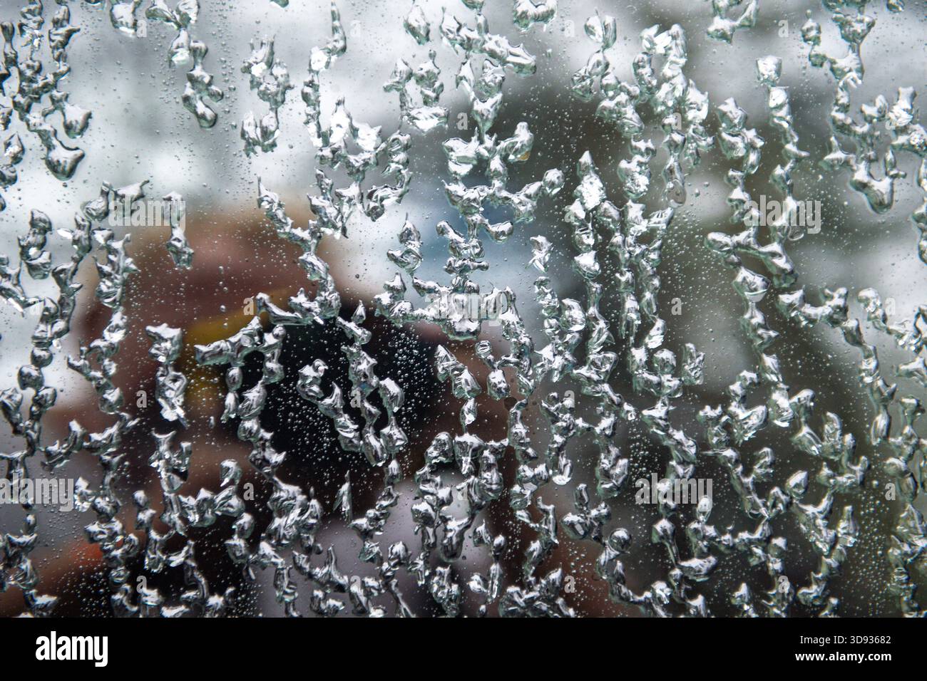 A window with frost and ice on it and a person's reflection in it. The reflection is blurry and the frost is intricate and detailed Stock Photo