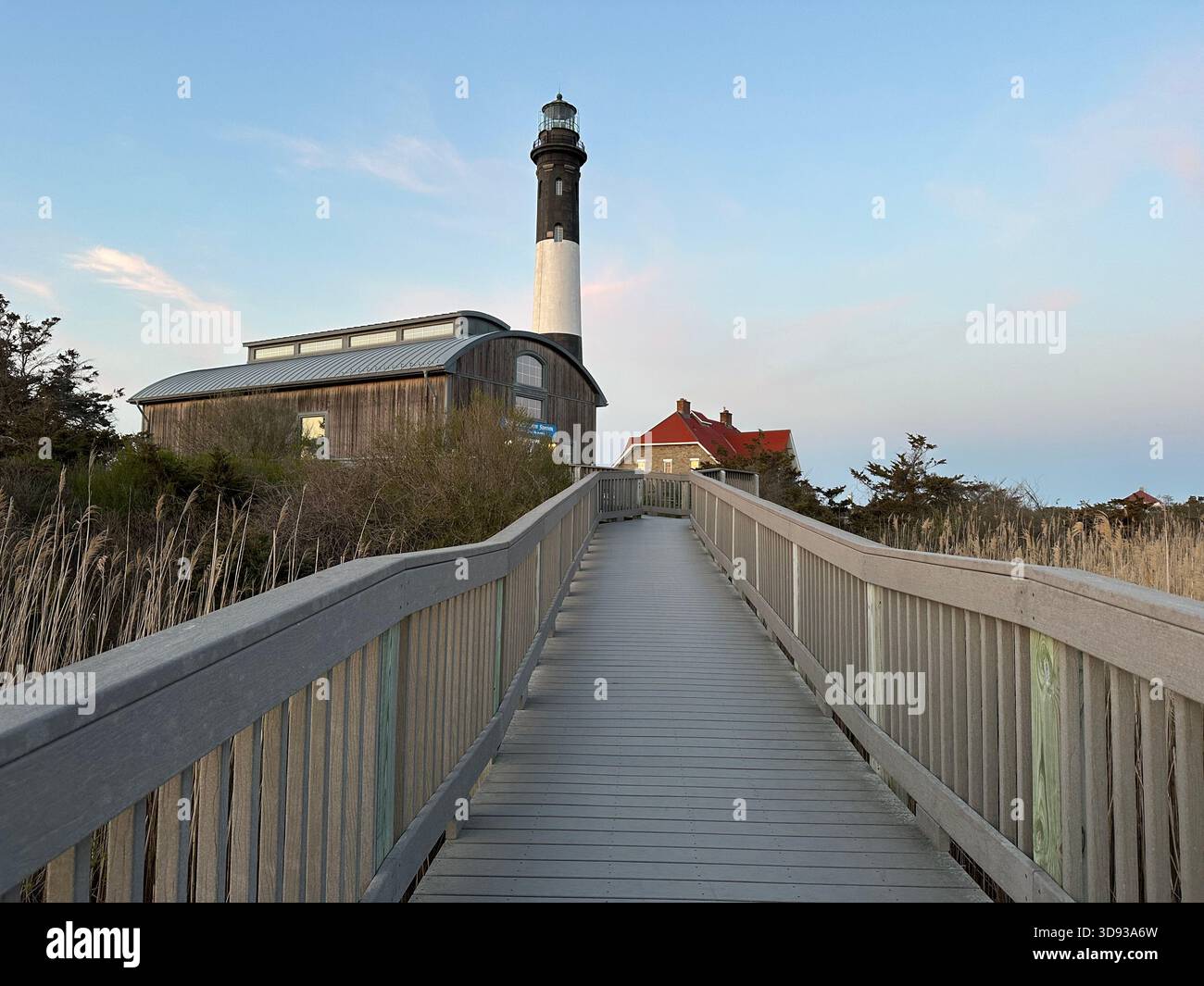 Wooden boardwalk leading to a coastal lighthouse on Long Island, New York, on a bright clear day by the shoreline. - Smartphone Captured Stock Image