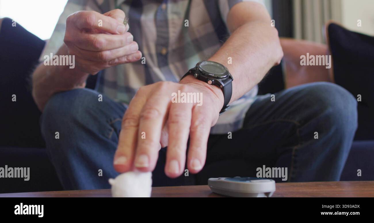 Handling lancet, senior male in plaid shirt, on sofa reaching cotton ball on table with glucometer Stock Photo