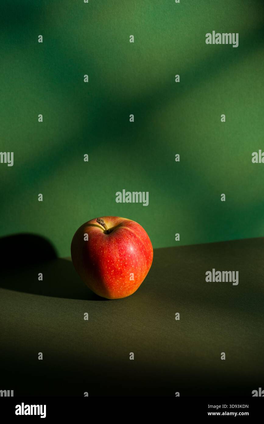Red apple on green background with window light effect. Stock Photo