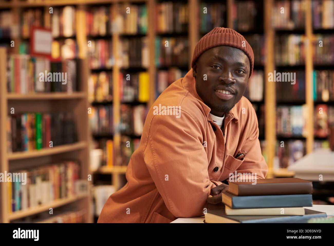 Portrait of Young Black Man Smiling While Leaning on Stack of Books Stock Photo