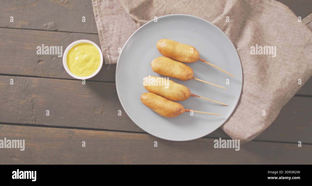 Presenting plate with four skewered corn dogs on dark tabletop, with mustard bowl and linen napkin Stock Photo