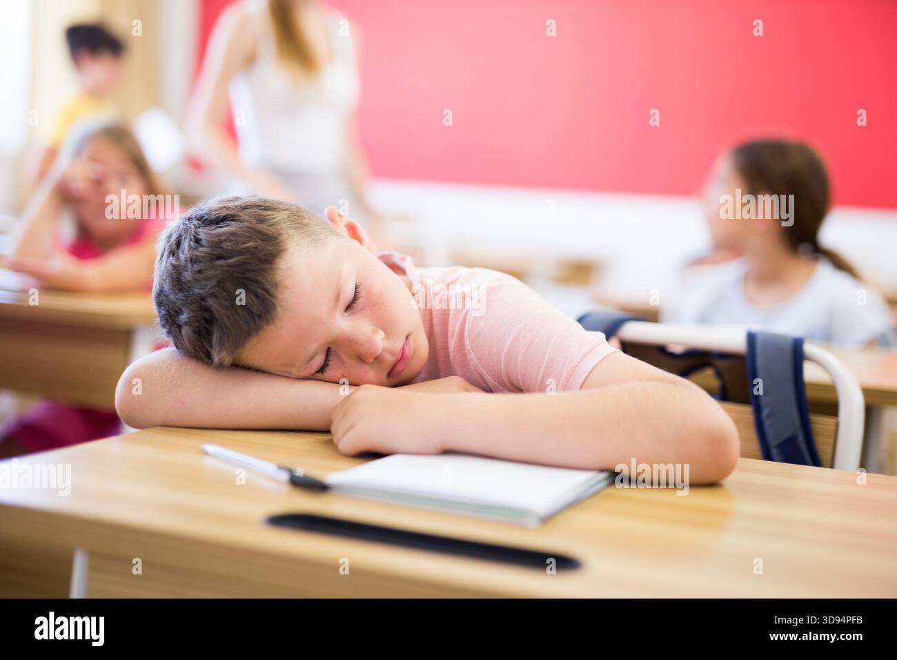 Bored tween boy sleeping at desk in classroom during lesson Stock Photo