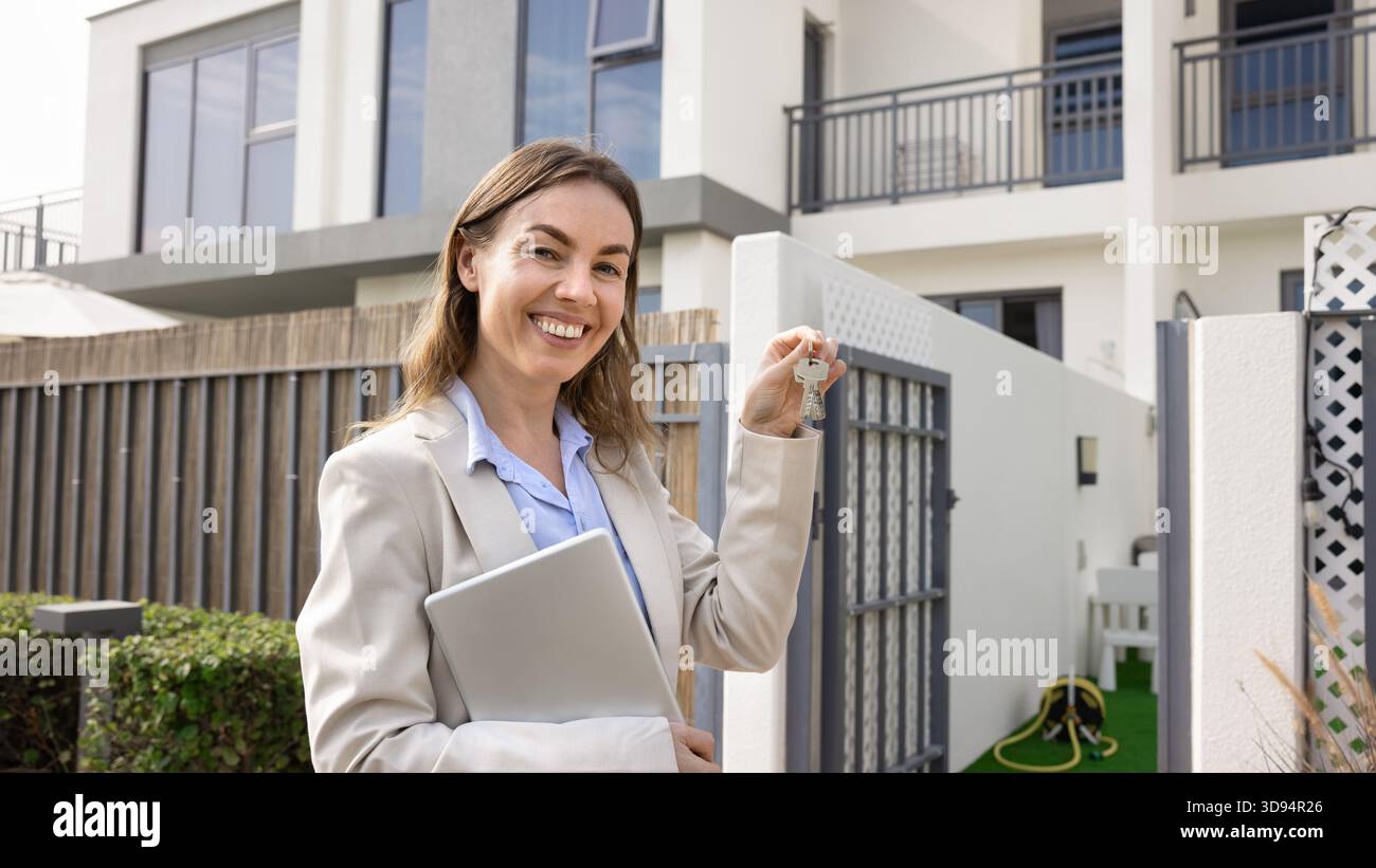 Smiling real estate agent with house keys posing outdoors Stock Photo