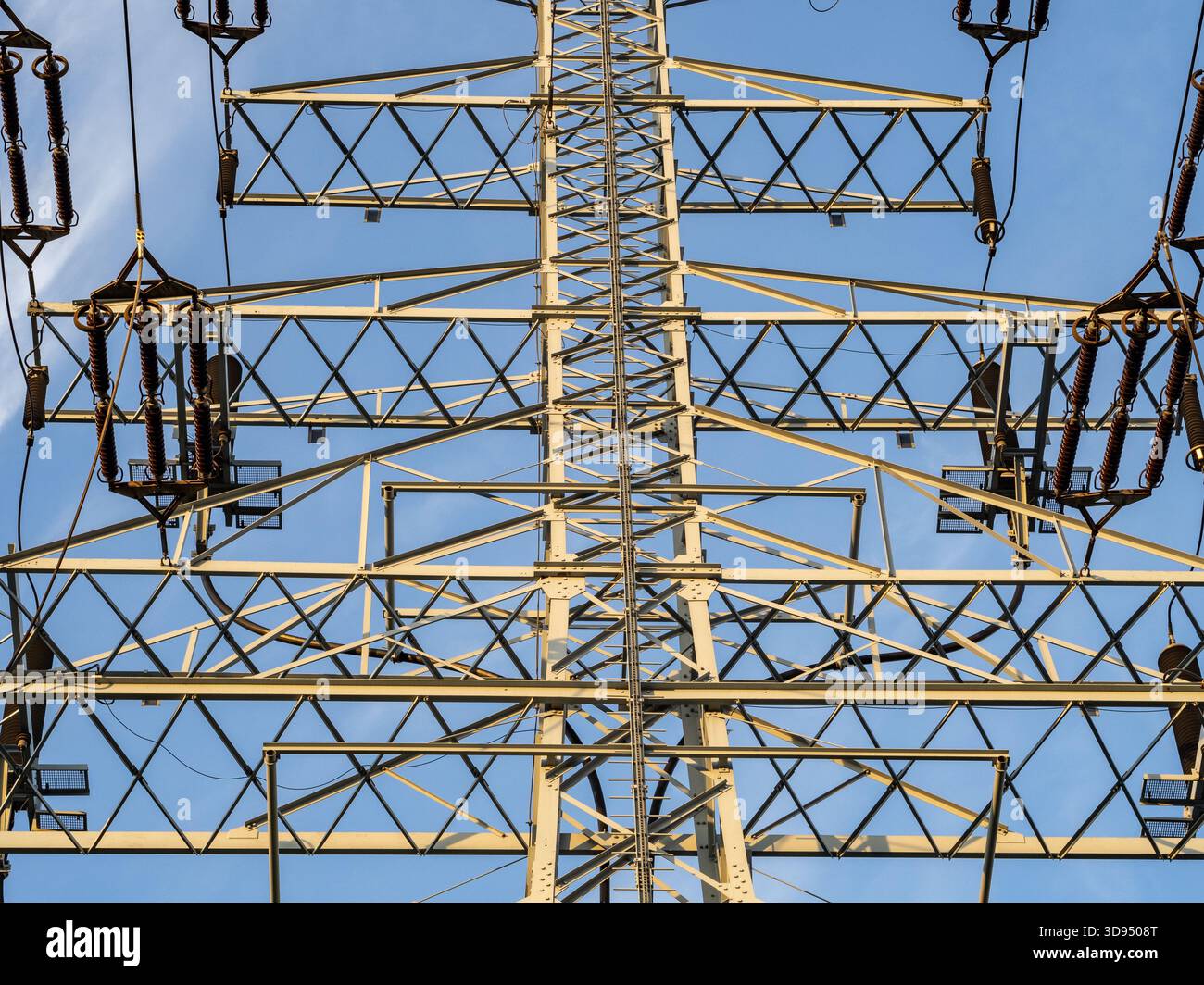 A towering power transmission tower stands against a clear blue sky ...