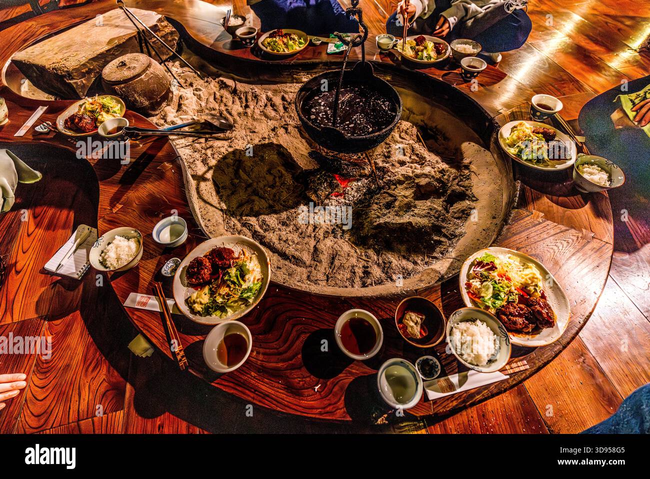 A top view of the circular irori in a traditional restaurant in Hakone, Kanagawa Prefecture, Japan: a cast-iron kettle (tetsubin) hangs over glowing embers in an ash pit; arranged around it are bowls of rice, steamed vegetables, tofu and other accompaniments for a Japanese meal. Irori cooking is one of Japan’s oldest cooking methods and is still practised mainly in mountainous regions Stock Photo