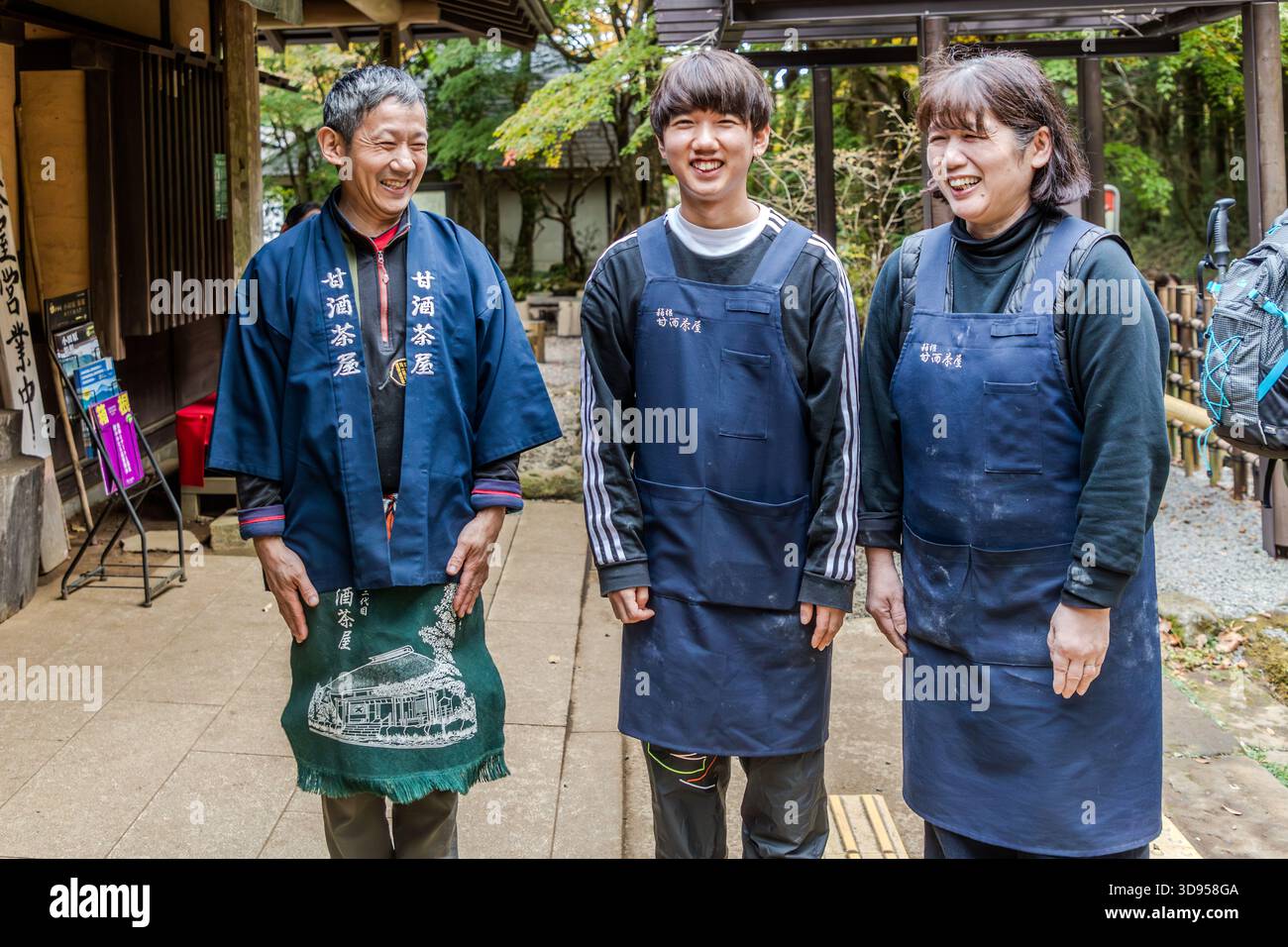 Three staff members of the Amazake Chaya (甘酒茶屋) in front of the entrance to the traditional teahouse on the historic Hakone Trail, Hakone, Kanagawa Prefecture, Japan. The establishment has been family-owned for several centuries and served as a resting place for travellers on the old Tōkaidō Stock Photo