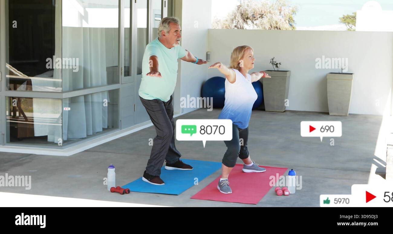 Practicing senior couple holding forward stance on covered patio in workout with mats, social icons Stock Photo